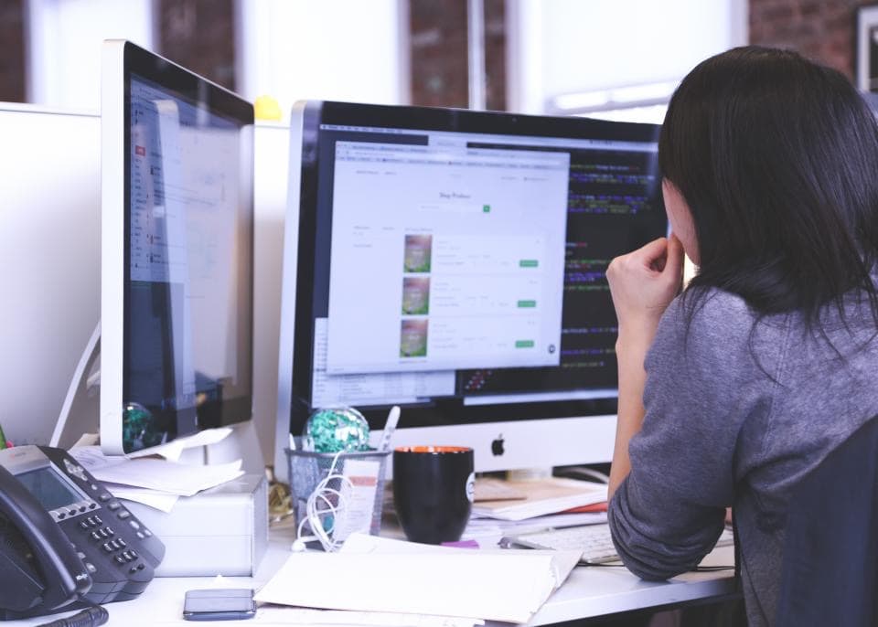 Analyste concentrée devant deux écrans affichant du code, représentant le travail d'un pré-audit de cybersécurité