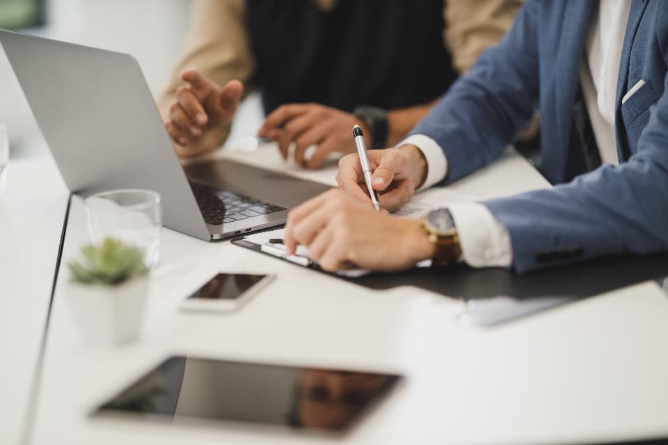 Two colleagues signing a document near a laptop, illustrating GDPR compliance work