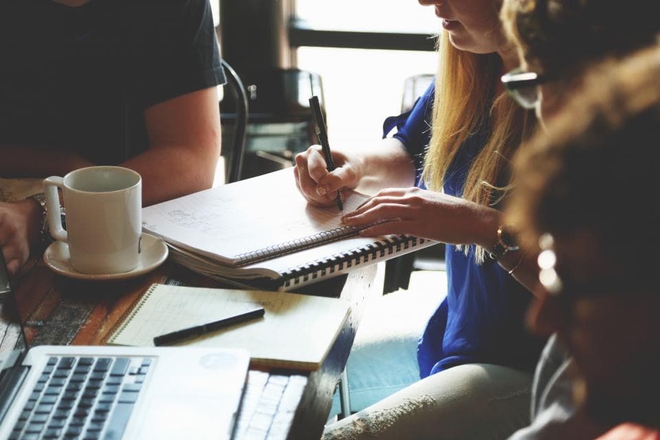 Équipe prenant des notes ensemble autour d'un café, illustrant les étapes de préparation d'une due diligence IT