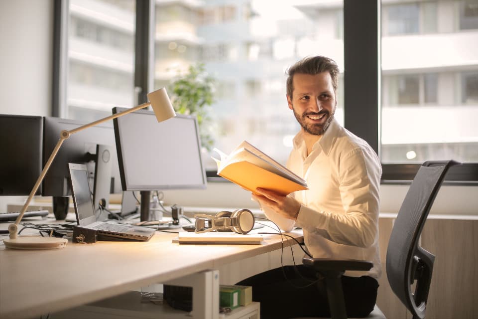 Smiling professional reviewing a binder at his desk, illustrating the drafting of a security policy (ISSP)